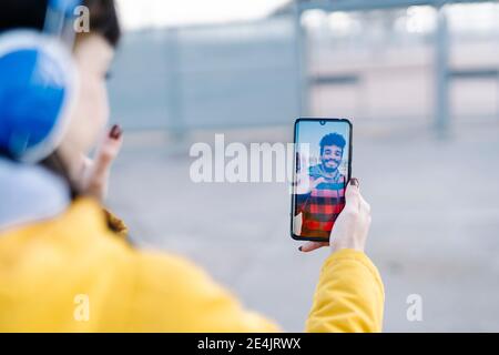 Young woman talking with friend on video call through mobile phone while standing outdoors Stock Photo