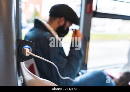 USB cable connected to electrical outlet while businessman in background in bus Stock Photo