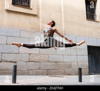 Dancer wearing leotard dancing while jumping with legs stretched on footpath Stock Photo