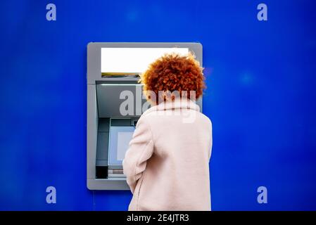 Mid adult woman with afro hair using kiosk in city Stock Photo