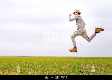 Young man jumping and posing mid-air in grassy field Stock Photo
