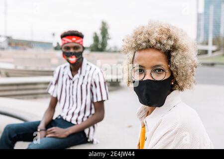 Man and woman wearing face mask staring while sitting on bench Stock Photo