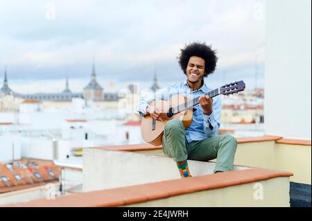 Young man with eyes closed playing acoustic guitar while sitting on terrace Stock Photo