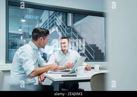 Smiling male professional looking at male colleague in boardroom at industry Stock Photo