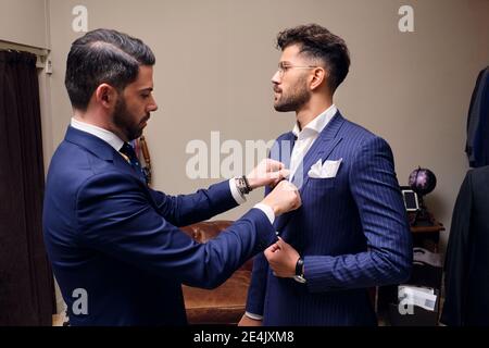 Tailor in his menswear store adjusting customers blue pinstripe suit Stock Photo