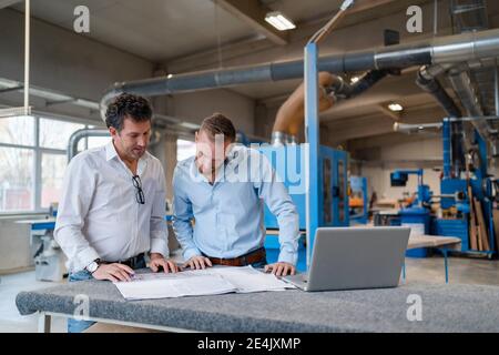 Two carpenters talking over documents in production hall Stock Photo