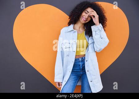 Young woman with eyes closed standing against heart shape on wall Stock Photo