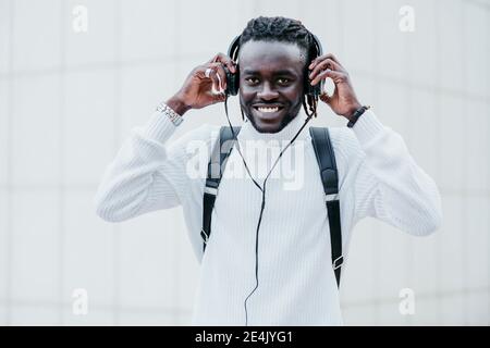 Happy man wearing headphones while standing against white wall Stock Photo