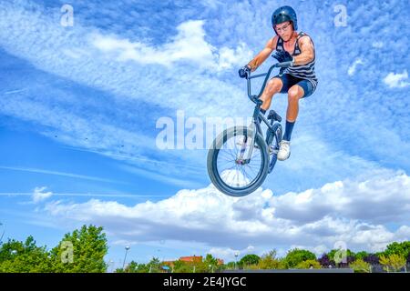 Young man with bicycle jumping against blue sky at bike park Stock Photo