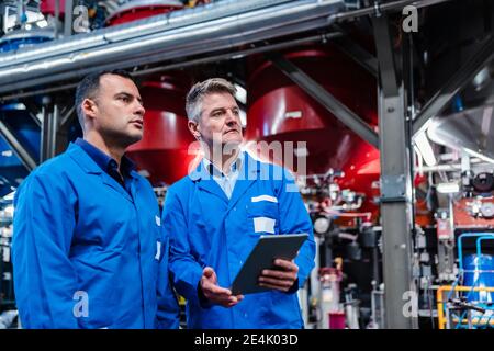 Multi ethnic technicians with digital tablet looking away while standing in industry Stock Photo
