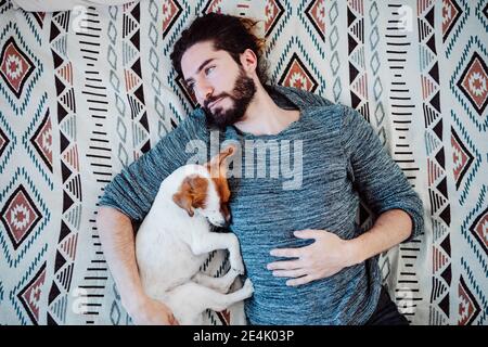 Thoughtful man lying on bed with dog at home Stock Photo