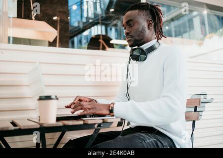 Creative businessman with disposable coffee cup working on laptop in cafe Stock Photo