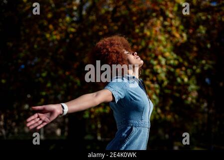 Mid adult woman with arms outstretched and eyes closed at public park