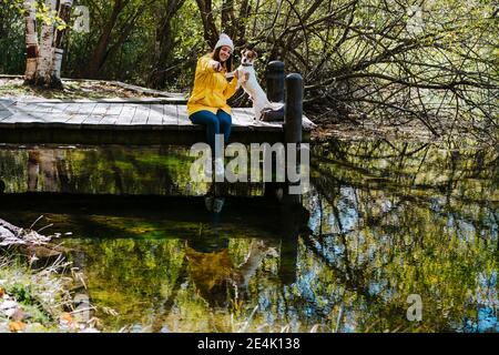 Woman with dog sitting on pier by lake in Autumn Stock Photo