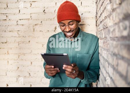 Happy man using digital tablet while leaning by brick wall Stock Photo
