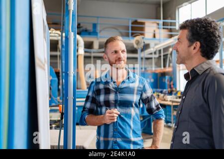 Two carpenters talking over documents in production hall Stock Photo