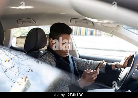Young man driving car and using smartphone Stock Photo