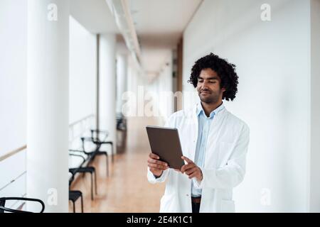 Confident young male doctor using digital tablet at hospital corridor Stock Photo