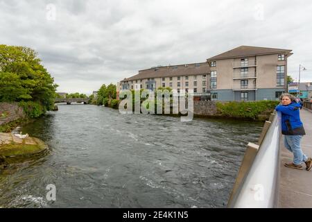 Tourist on the Wolfe Tone Bridge over the Corrib River admiring the landscape, buildings and the William O'Brien Bridge in the background, cloudy day Stock Photo