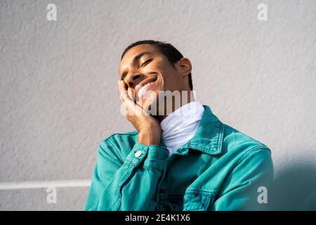 Smiling man standing with eyes closed against gray wall Stock Photo