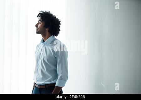 Thoughtful young handsome male professional looking away while standing at office Stock Photo