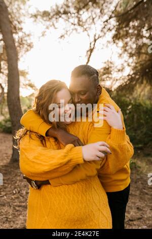 Happy boyfriend hugging girlfriend while standing at forest Stock Photo