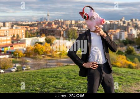 Thoughtful male professional wearing pig mask and wireless headphones against sky Stock Photo