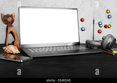 Workspace: modern laptop computer blank isolated white screen, mobile smartphone, headphones, pen, pencil, cat figurine, seashell, decor, black wooden Stock Photo