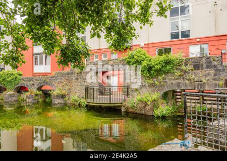 Old stone wall with arches and a small balcony with metal railing and a modern building in the background, canal with reflection in the water, cloudy Stock Photo