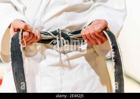 Close-up of mature man tying black belt on waist in club Stock Photo