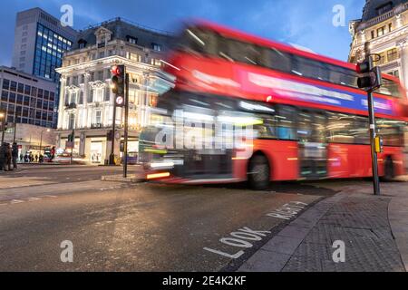 UK, London, Red double decker bus crossing Oxford Circus junction at night, blurred