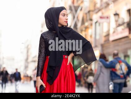 Portrait of young woman wearing black hijab posing outdoors with hand on hip Stock Photo