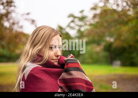Young woman wrapped in scarf at park during autumn Stock Photo