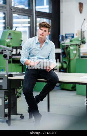 Male engineer with document looking away while siting on desk in industry Stock Photo