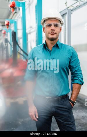 Male engineer with hands in pockets standing in factory Stock Photo