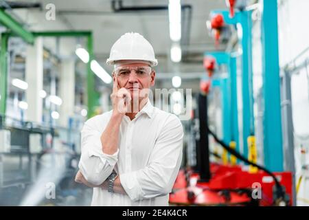 Thoughtful mature engineer wearing protective workwear while standing in industry Stock Photo