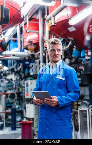 Mature engineer looking away while holding digital tablet in factory Stock Photo
