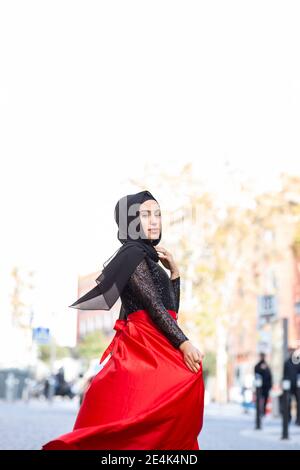 Portrait of young beautiful woman wearing hijab and long skirt posing in middle of city street Stock Photo