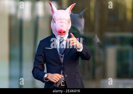Male professional gesturing wearing pig mask while standing against glass Stock Photo