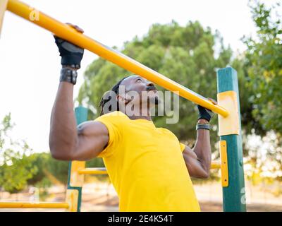 Male athlete doing chin-ups while exercising on road at park Stock Photo