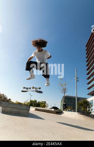 Young sportsman practicing kickflip with skateboard on sunny day Stock Photo
