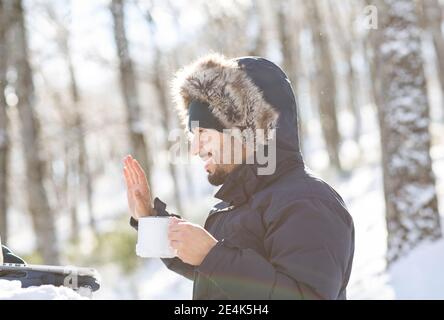 Smiling male entrepreneur gesturing on video call while having coffee in winter Stock Photo