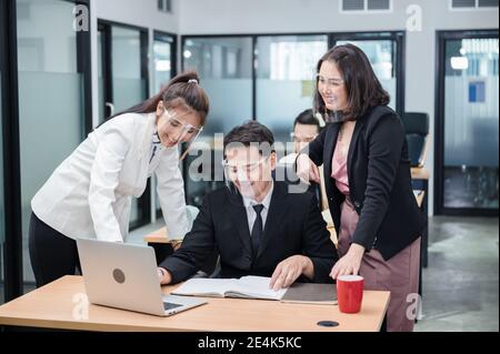 Woman manager and employees wearing medical face shield are discussing on desk in modern office while pandemic of Covid-19, Coronavirus Stock Photo