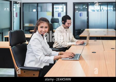 Young asian operator woman agent with headsets and colleagues working customer service in a call center Stock Photo
