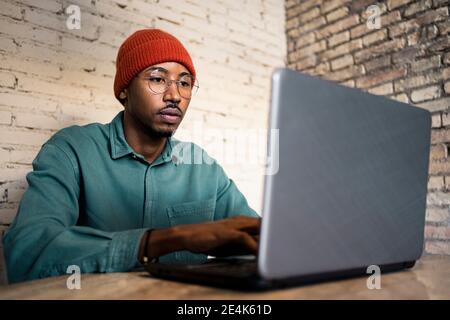 Businessman working on laptop against brick wall at table Stock Photo