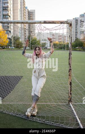 Hipster female leaning on net of soccer goalpost in city Stock Photo