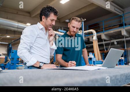 Two carpenters talking over documents in production hall Stock Photo