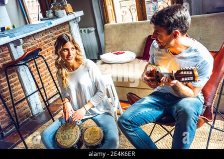 Young couple playing duet with drums and guitar in living room at home Stock Photo