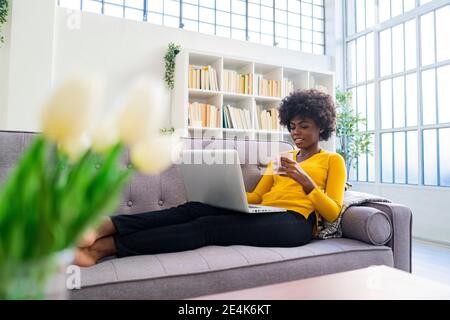Woman drinking coffee while working on laptop at home Stock Photo
