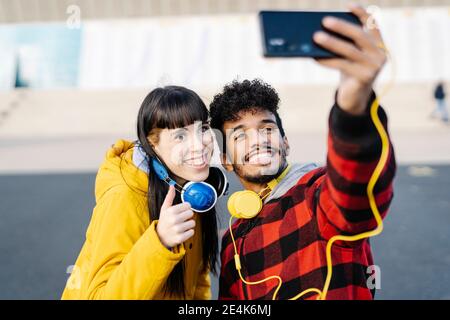 Young man taking selfie through mobile phone with female friend while standing outdoors Stock Photo